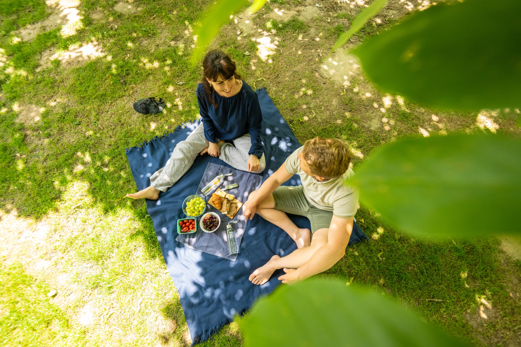 Mann und Frau sitzen auf einer Decke im Bürgerpark und Picknicken