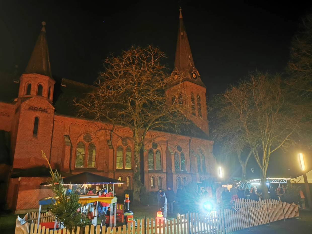 © Ummelner Gemeinschaft e. V. Ummelner Kirche im Dunkeln, davor Weihnachtsmarktstände und Menschen