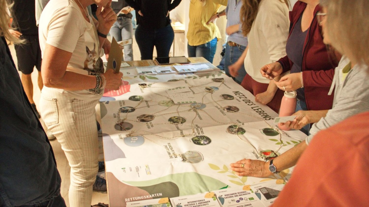 Spielplan auf Tisch liegend, Kinder stehen drum herum