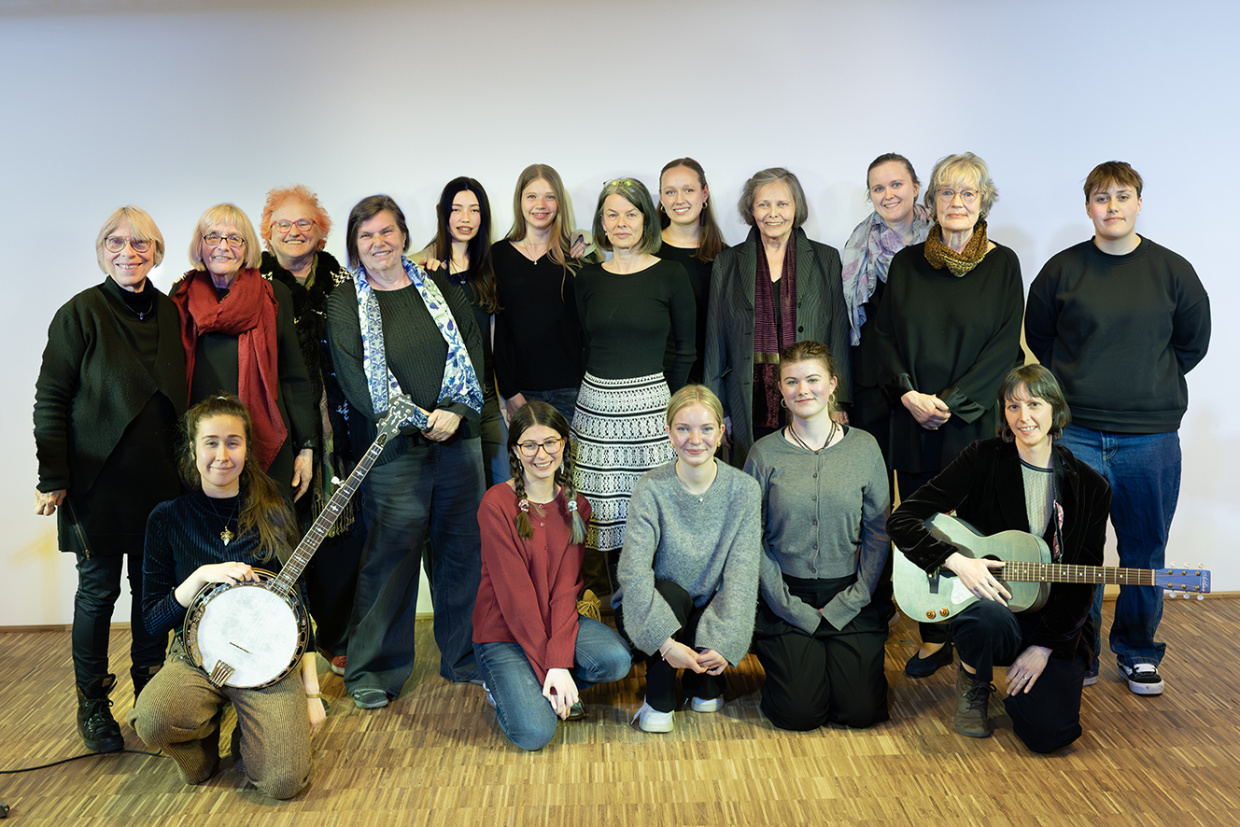 Gruppe von etwa 15 Personen in Businesskleidung posiert gemeinsam für ein Gruppenfoto vor weißer Wand.