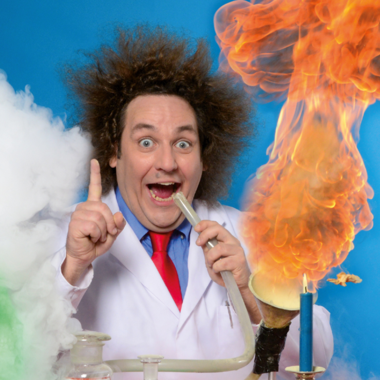 Auf dem Bild ist ein Mann mit hochstehenden Haaren zu sehen. Er hat den Mund auf, den Zeigefinger gehoben. Er trägt eine weißen Forscherkittel. Rechts von ihm ist Rauch, Links eine Flamme.