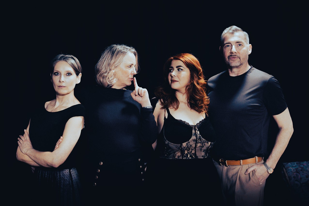 Vier Personen stehen vor dunklem Hintergrund in Porträtpose nebeneinander.