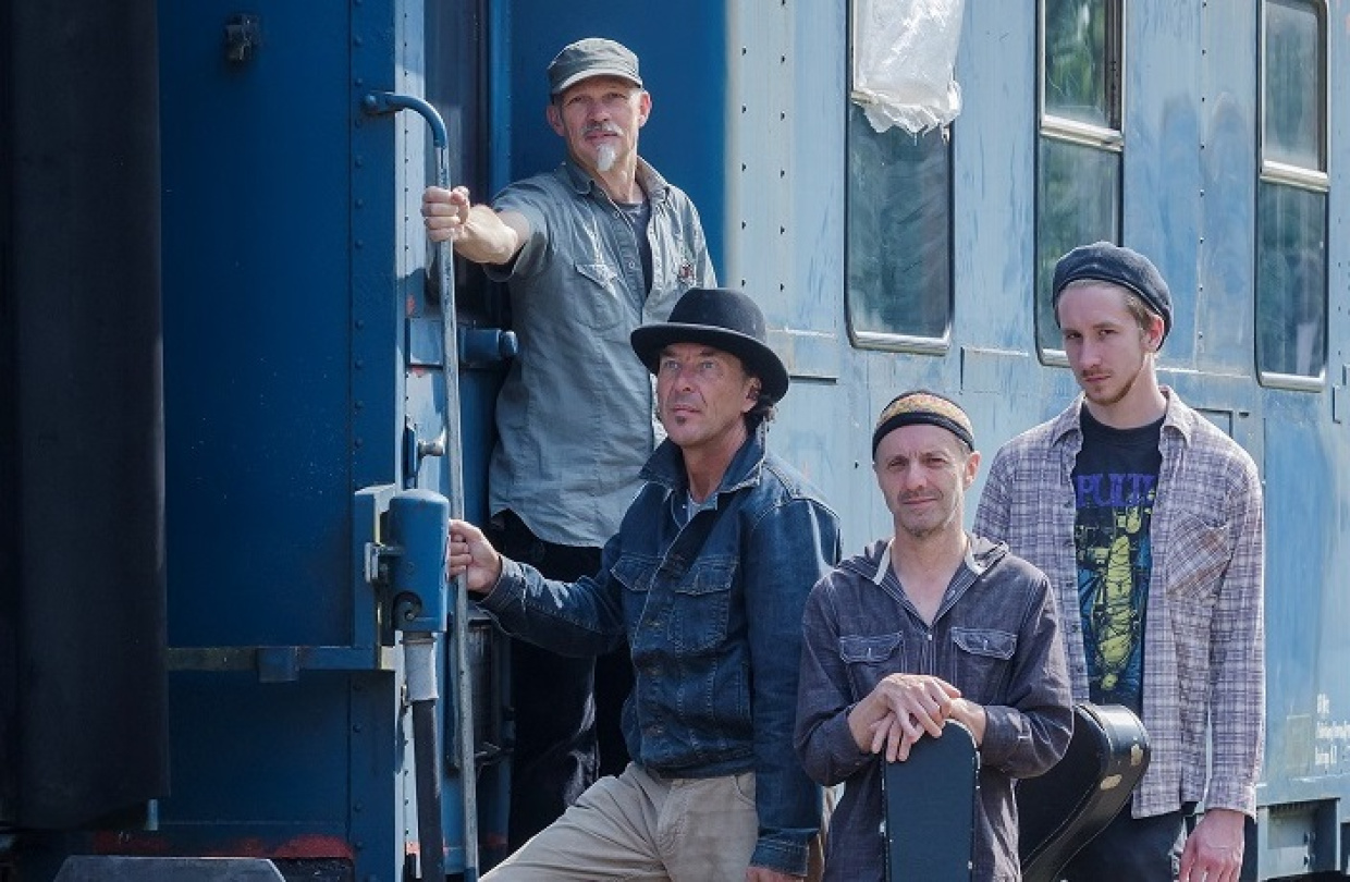 Vier Männer an einem Bahnwagon mit ihren Instrumenten