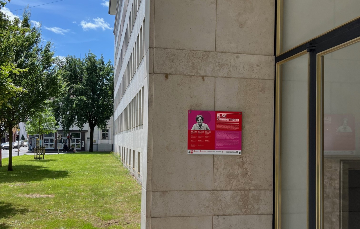 Rotes Schild an Betonwand neben grüner Wiese und Gebäude.