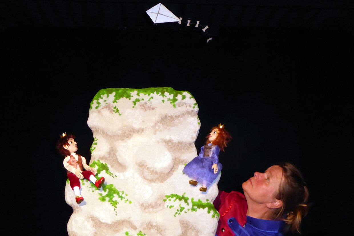 Zwei Kinder sitzen auf einem Berg und lassen einen Drachen steigen