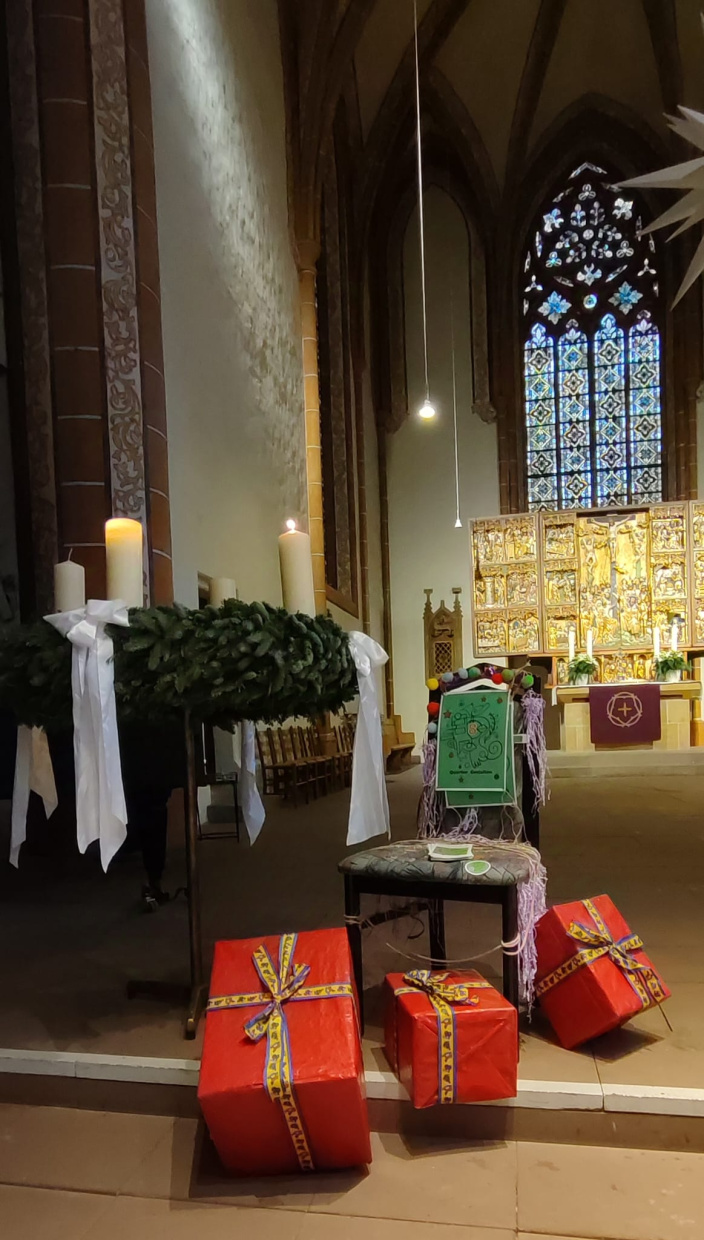 Altarraum mit Adventskranz, Geschenken und einem gestalteten Stuhl mit Nummer