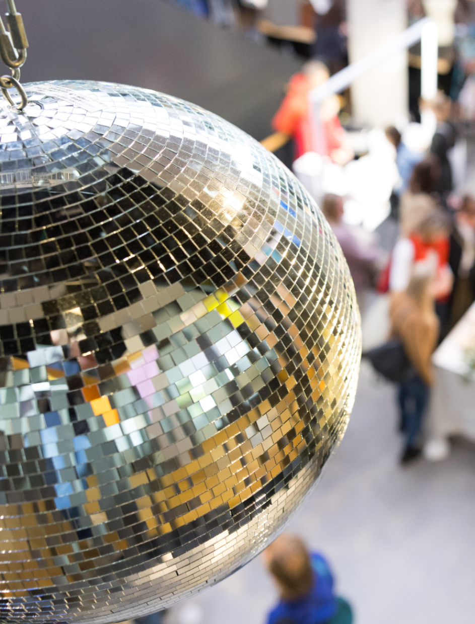 Discokugel von oben, im Hintergrund (unscharf): buntes Treiben während einer Veranstaltung