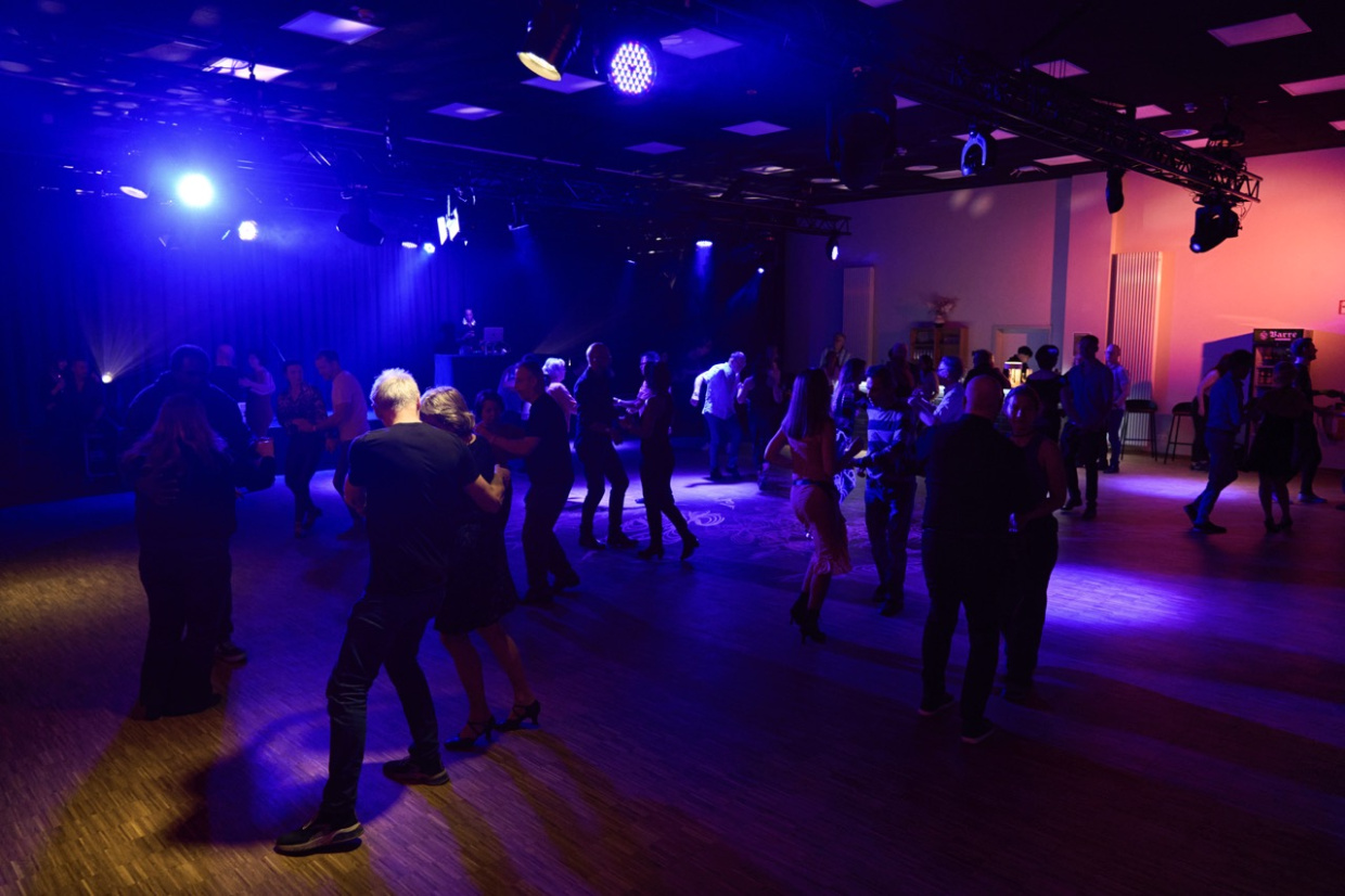 Das Bild zeigt tanzende Menschen auf einer bunt beleuchteten Tanzfläche.