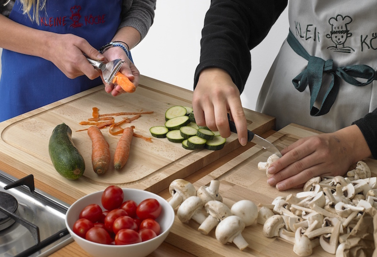 Zwei Kinder mit Schürzen schneiden und schälen auf Holzschneidebrettern Gemüse