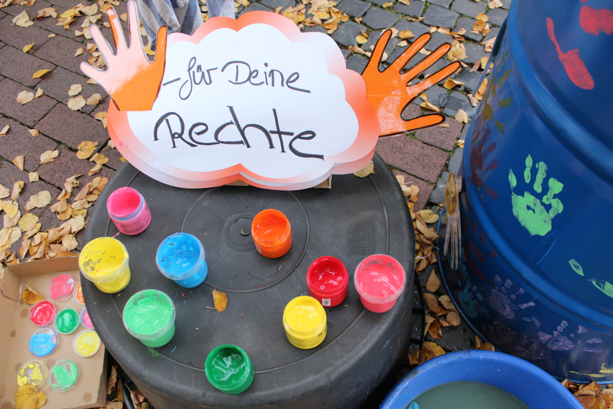 Auf einem Schild steht "Kinder haben Rechte". Darunter stehen bunte Farbtöpfe.