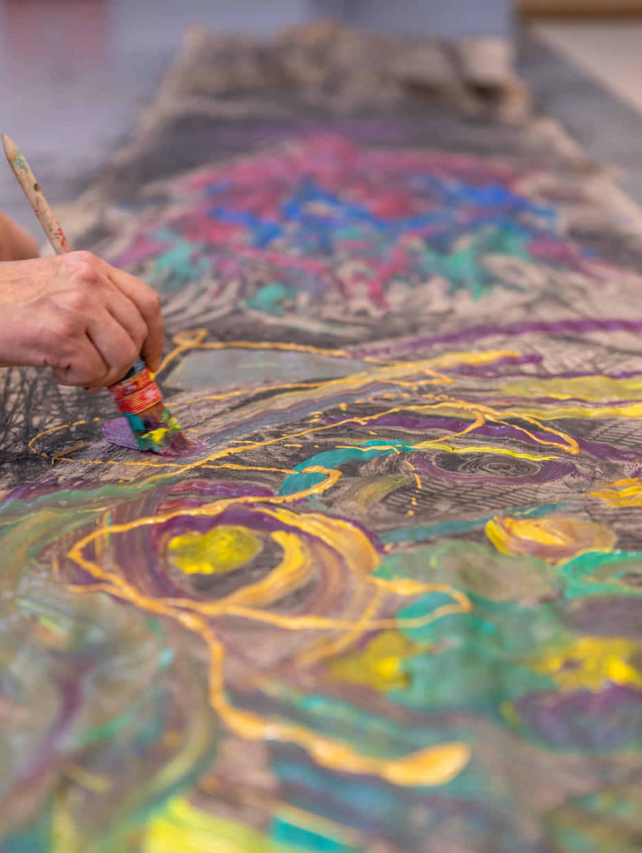 eine Hand mit einem Pinsel malt mit Farben über eine Papierbahn