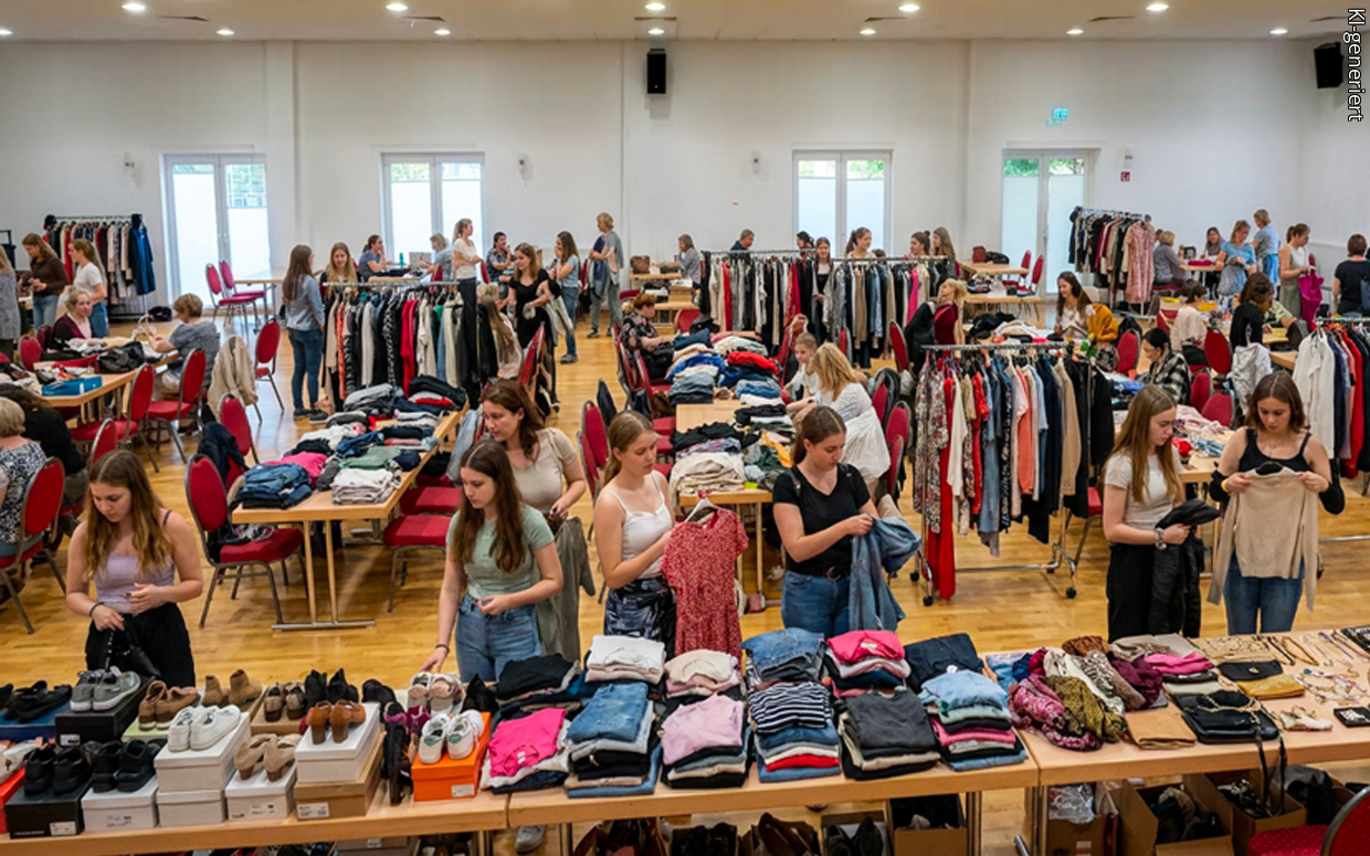 Heller Saal mit Verkaufstischen und Kleiderstangen, darauf diverse Kleidung, Schuhe und Accessoires
