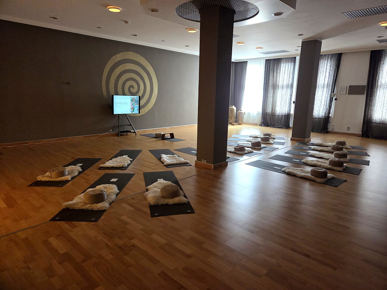 Großer Raum im yogawirkt mit Matten, Fellen und Kissen, an der Wand eine goldene Spirale