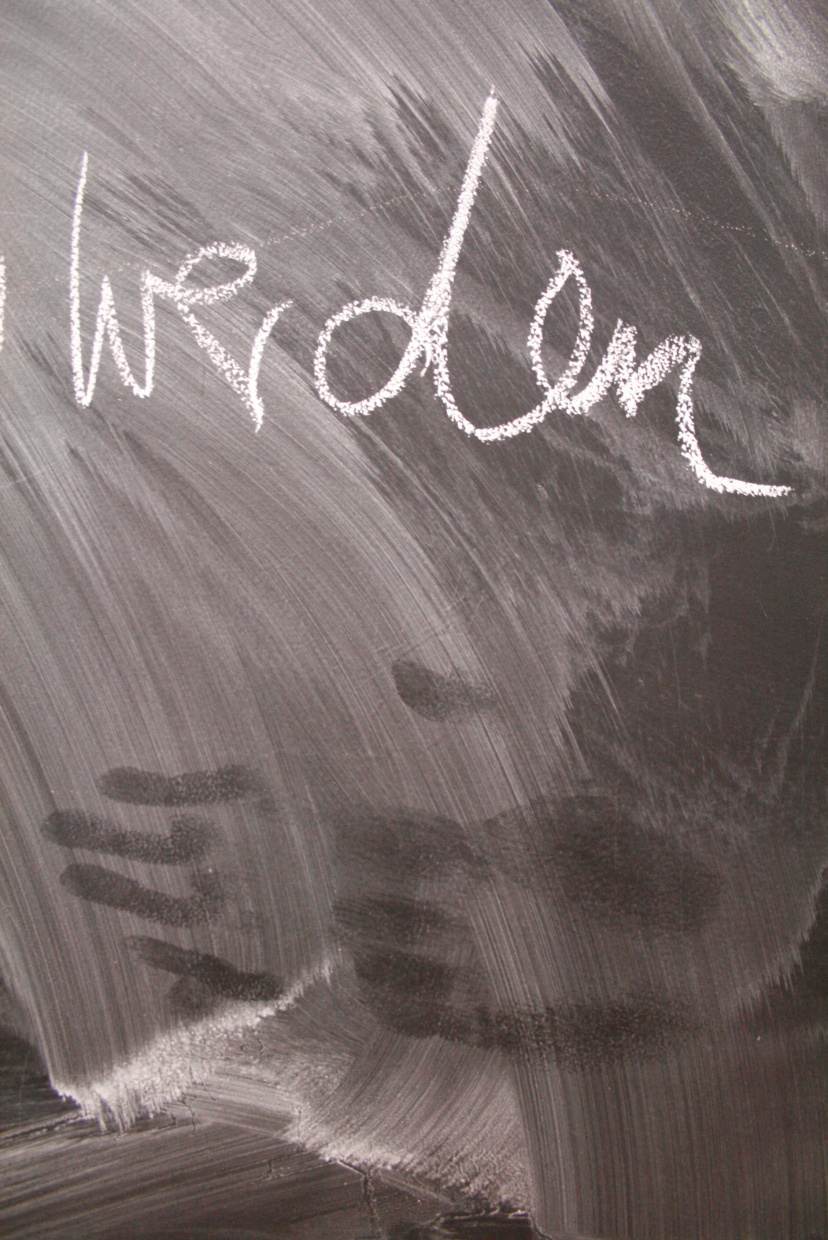 auf einer Tafel steht das Wort "werden" geschrieben, darunter sind Spuren von Händen zu sehen