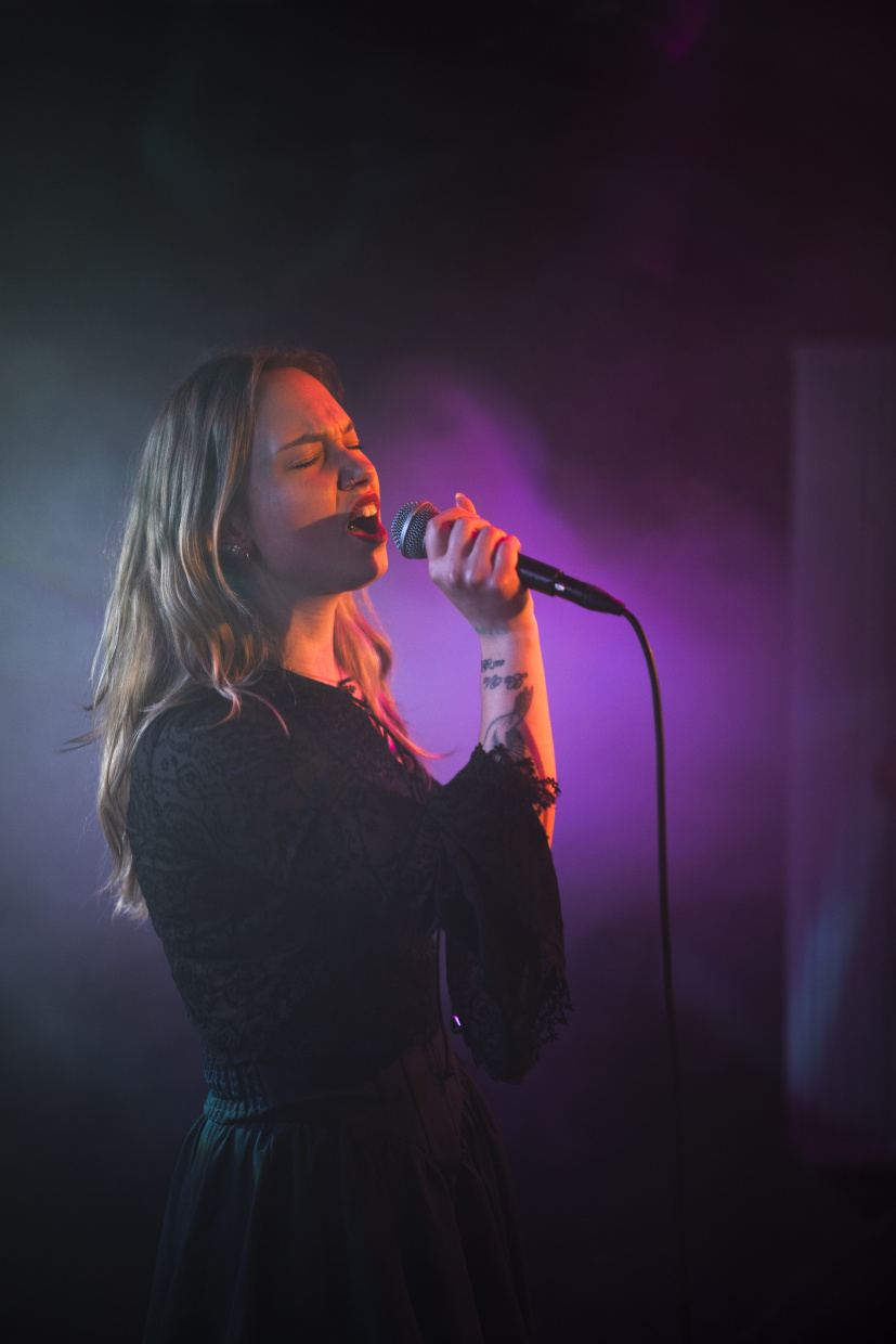Sängerin singt mit geschlossenen Augen ins Mikrofon, Bühne im violetten Licht mit Nebel.