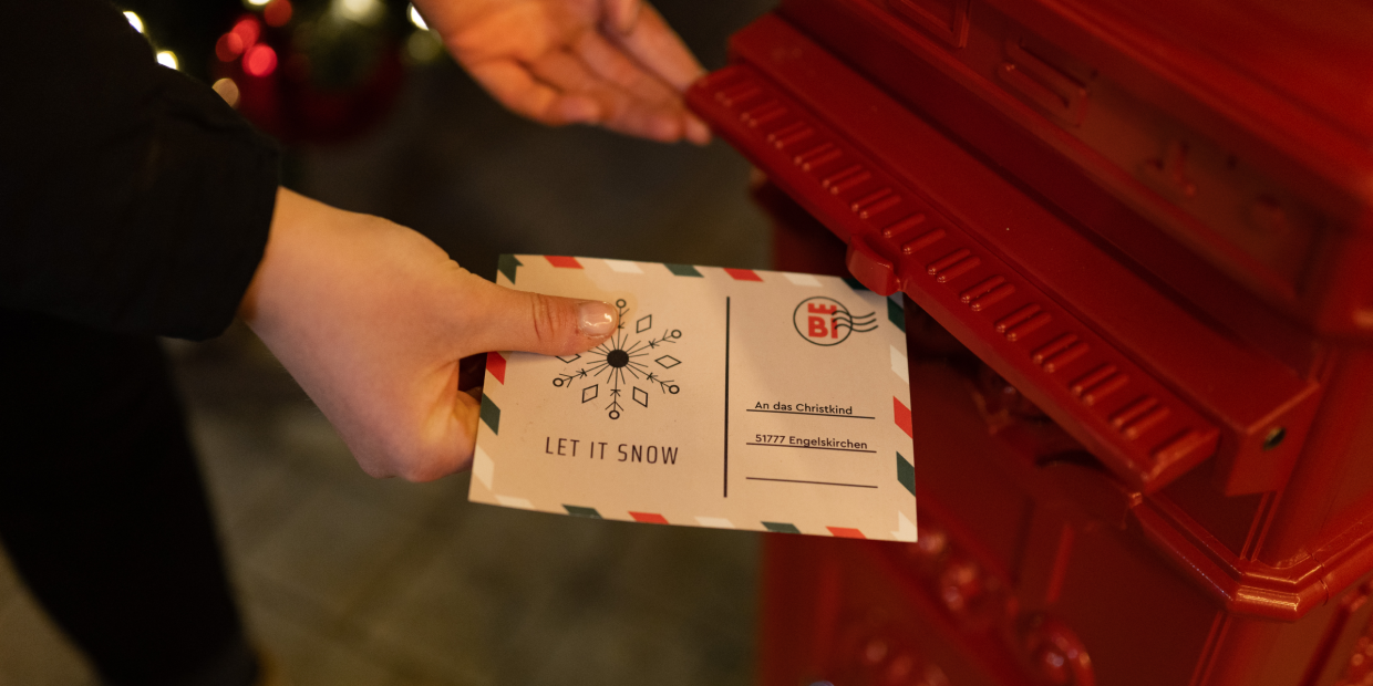 Hände werfen einen Brief ans Christkind in einen roten Briefkasten