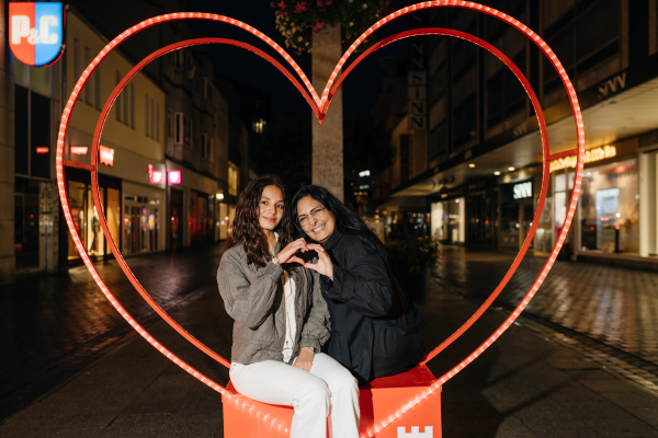 zwei Frauen sitzen in einem Herzrahmen und formen ihre Hände zu einem Herz