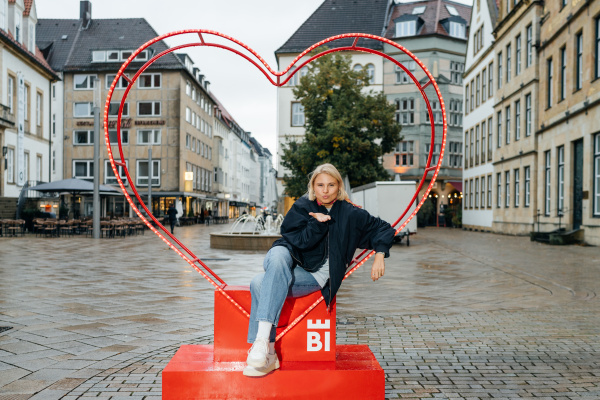 eine junge Frau sitzt in einem Herzrahmen und verteilt einen Luftkuss