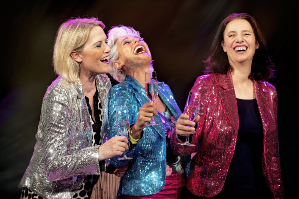 Drei lachende Frauen in bunten Glitzer-Sakkos mit Sektgläsern in der Hand