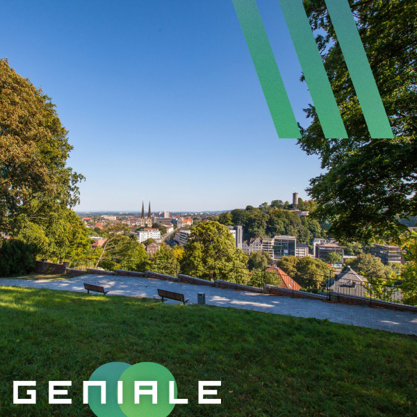 Links und rechts sind Bäume zu sehen, nach vorne heraus Rasen und die Bielefelder Skyline von der Sparrenburg aus.