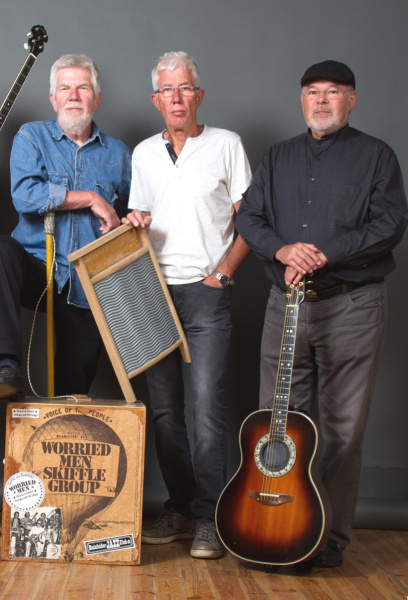 Drei ältere Musiker stehen mit Gitarre und Waschbrett in einem raum mit Holzfußboden