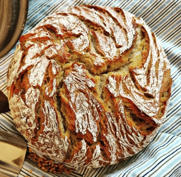 Ein rundes ganzes Brot von oben gesehen, welches mit Mehl bestäubt ist.