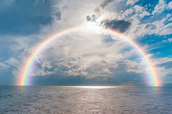 Auf dem Bild ist ein Regenbogen über dem Meer zu sehen.