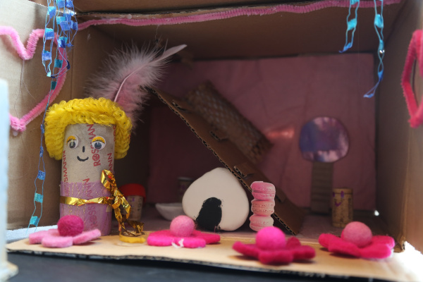 ein Pappkarton gestaltet mit einer Figur, pinkfarbenen Blüten und einem Bild von Macarons