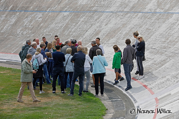 Eine Besuchergruppe vor einer Steilkurve der Radrennbahn