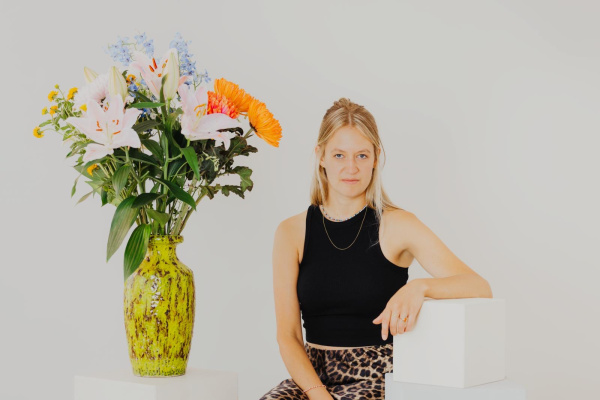 Portraitfoto der Autorin vor hellem Hintergrund neben einem großen Blumenstrauß
