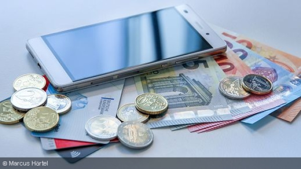 Smartphone liegt auf Euro-Banknoten und -Münzen.