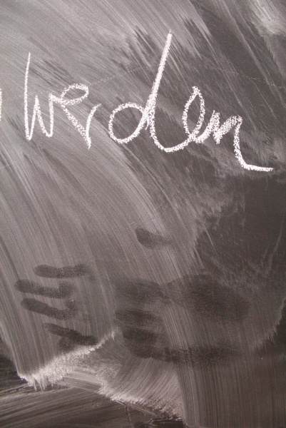 auf einer Tafel steht das Wort "werden" geschrieben, darunter sind Spuren von Händen zu sehen