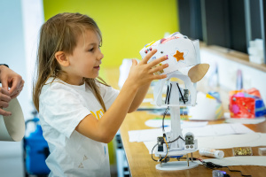 Kind gestaltet eine Roboterfigur mit Bastelmaterial, Sternaufklebern und Elektronikbauteilen.